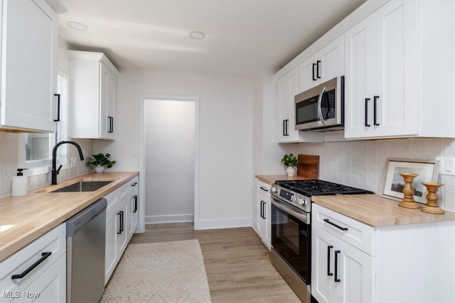 kitchen with white cabinetry, light hardwood / wood-style flooring, butcher block countertops, stainless steel appliances, and sink