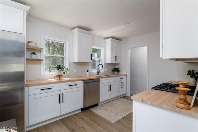 kitchen with white cabinetry, butcher block counters, stainless steel appliances, and sink