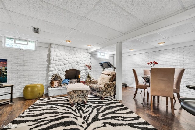 interior space with a fireplace, dark wood-type flooring, brick wall, and a drop ceiling