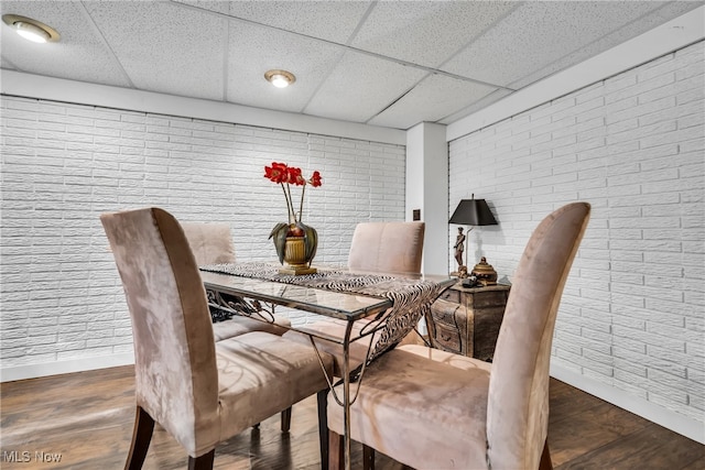 dining space featuring dark hardwood / wood-style floors, a drop ceiling, and brick wall