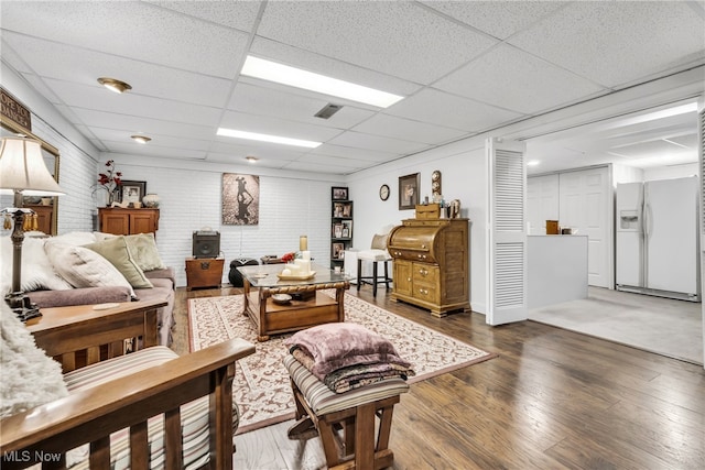 living room featuring dark wood-type flooring, a paneled ceiling, and brick wall