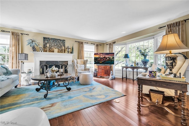 living room with crown molding, a tiled fireplace, and wood-type flooring