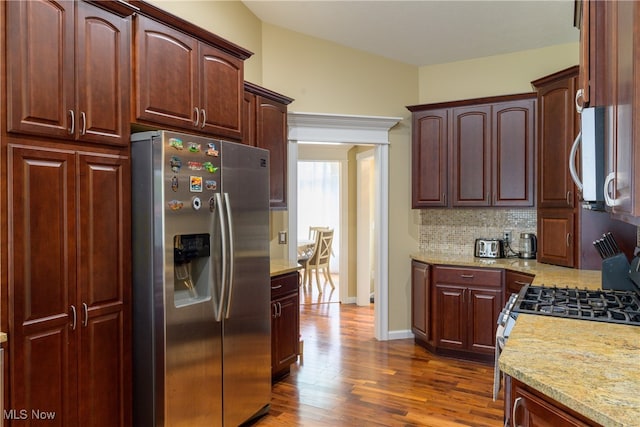 kitchen with dark wood-type flooring, light stone counters, stainless steel fridge, and backsplash