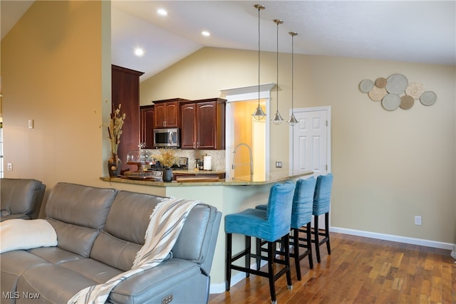 kitchen with pendant lighting, a kitchen breakfast bar, dark hardwood / wood-style flooring, kitchen peninsula, and decorative backsplash