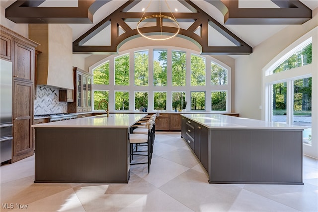 kitchen with tasteful backsplash, custom exhaust hood, sink, a large island, and high vaulted ceiling