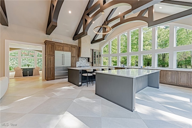 kitchen with stainless steel built in refrigerator, tasteful backsplash, a large island, high vaulted ceiling, and a breakfast bar area