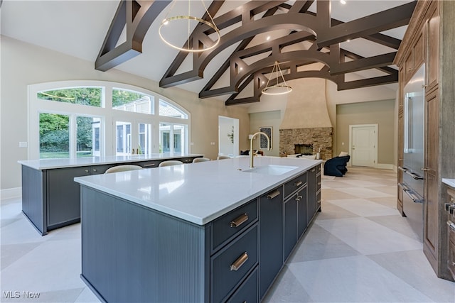 kitchen featuring high vaulted ceiling, a fireplace, sink, and a center island with sink