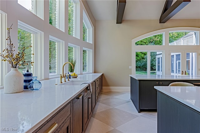 kitchen featuring a healthy amount of sunlight, sink, light stone counters, and beamed ceiling