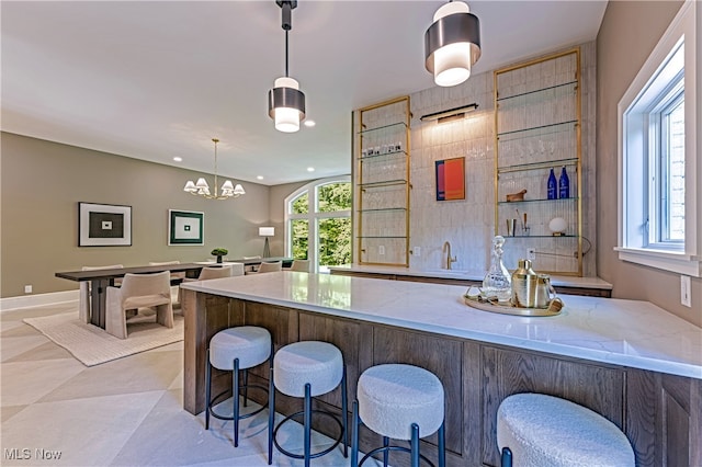 kitchen with light stone countertops, a breakfast bar, pendant lighting, and light tile patterned floors