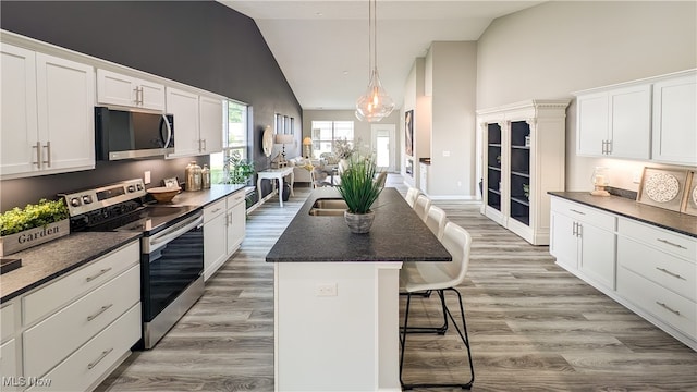 kitchen featuring white cabinets, a breakfast bar, appliances with stainless steel finishes, a center island, and light hardwood / wood-style floors