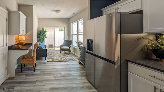 kitchen featuring white cabinets, stainless steel refrigerator with ice dispenser, light hardwood / wood-style floors, and a textured ceiling