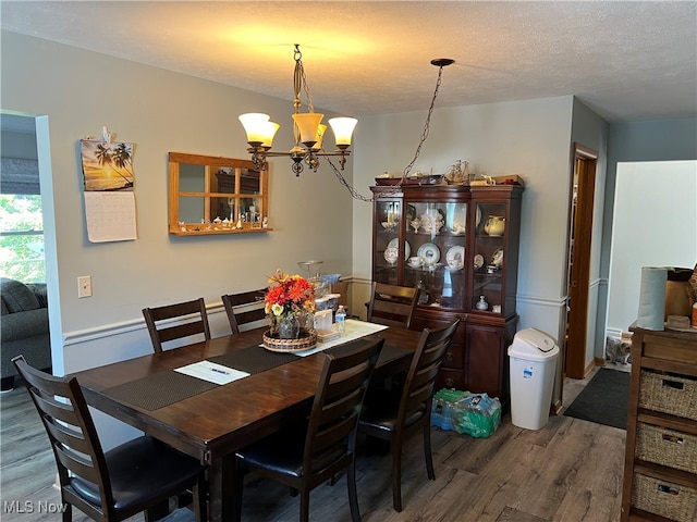 dining area with dark wood-type flooring, an inviting chandelier, and a textured ceiling