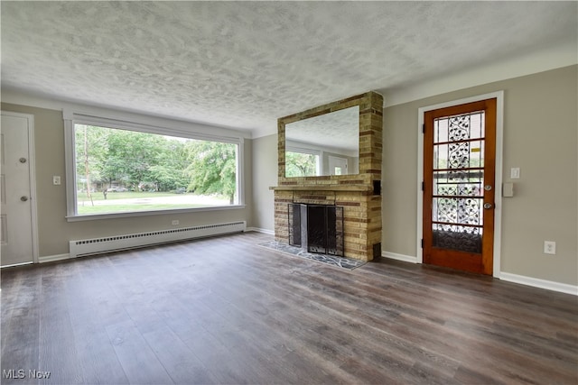 unfurnished living room featuring hardwood / wood-style flooring, a textured ceiling, baseboard heating, and a brick fireplace