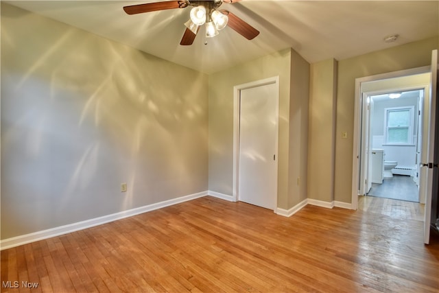 empty room featuring light wood-type flooring, ceiling fan, and baseboard heating