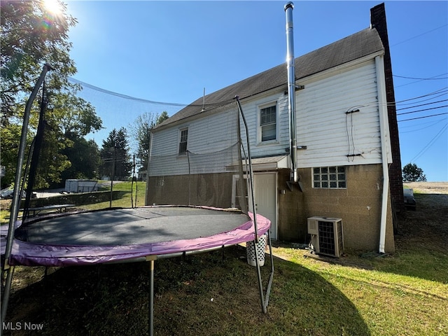 rear view of house with a lawn, cooling unit, and a trampoline