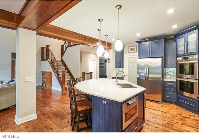 kitchen with a breakfast bar area, pendant lighting, hardwood / wood-style floors, a kitchen island with sink, and stainless steel appliances