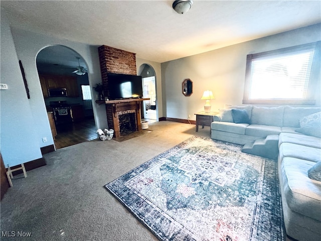 carpeted living room featuring a brick fireplace, ceiling fan, and a textured ceiling