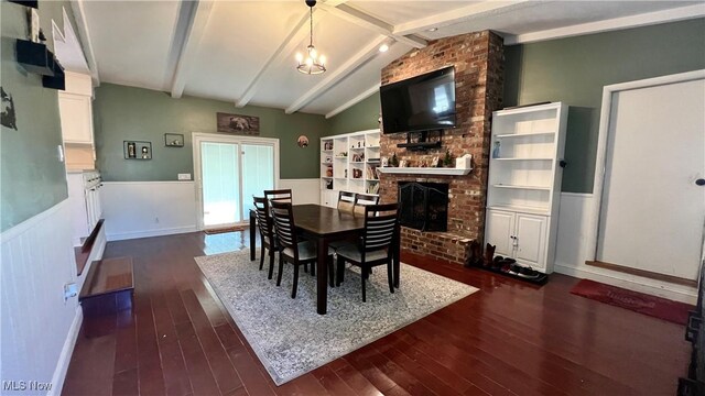 dining area with dark hardwood / wood-style floors, a brick fireplace, vaulted ceiling with beams, and a notable chandelier