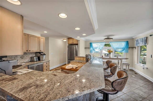 kitchen with ornamental molding, kitchen peninsula, backsplash, appliances with stainless steel finishes, and a breakfast bar