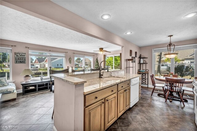 kitchen with pendant lighting, dishwasher, sink, an island with sink, and ceiling fan