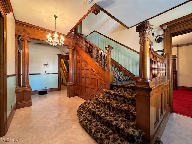 stairway featuring a notable chandelier, ornamental molding, and ornate columns