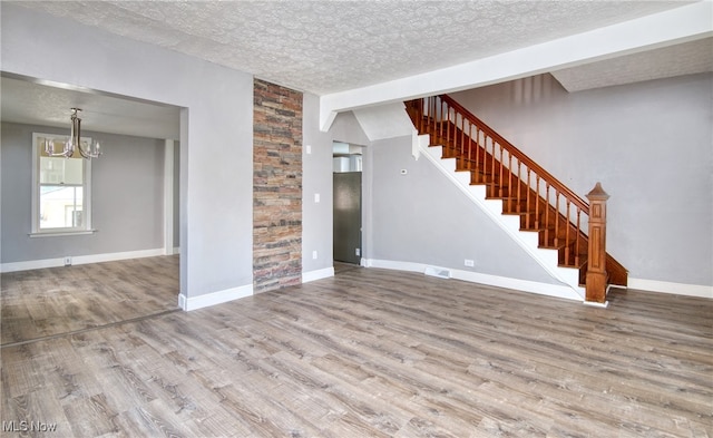 unfurnished living room with a textured ceiling, hardwood / wood-style floors, a chandelier, and lofted ceiling