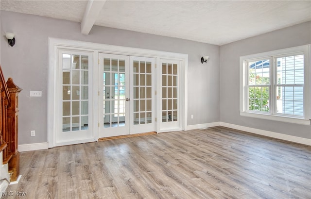 interior space featuring french doors, a textured ceiling, beamed ceiling, and light hardwood / wood-style flooring