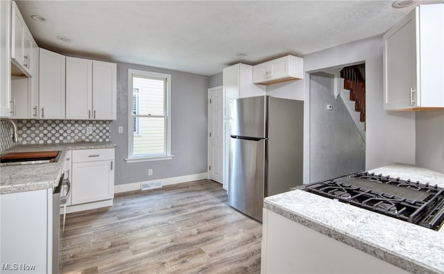 kitchen featuring white cabinets, stainless steel fridge, sink, and light hardwood / wood-style flooring