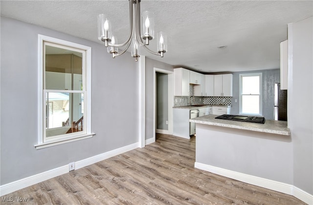 kitchen with light wood-type flooring, appliances with stainless steel finishes, white cabinetry, pendant lighting, and a textured ceiling