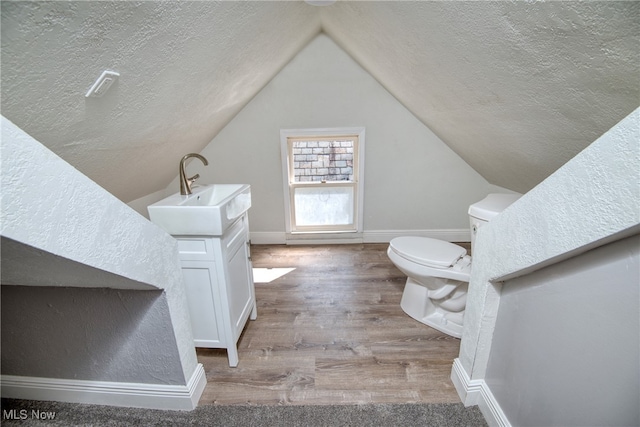 bathroom featuring a textured ceiling, vaulted ceiling, hardwood / wood-style floors, toilet, and vanity