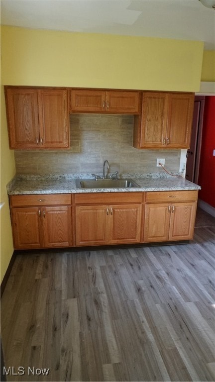 kitchen featuring light stone counters, dark wood-type flooring, backsplash, and sink