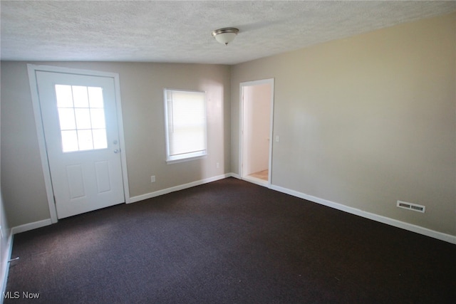 interior space with dark colored carpet, lofted ceiling, and a textured ceiling