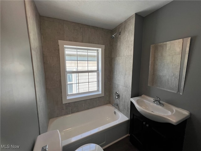 full bathroom featuring tiled shower / bath, vanity, toilet, and a textured ceiling