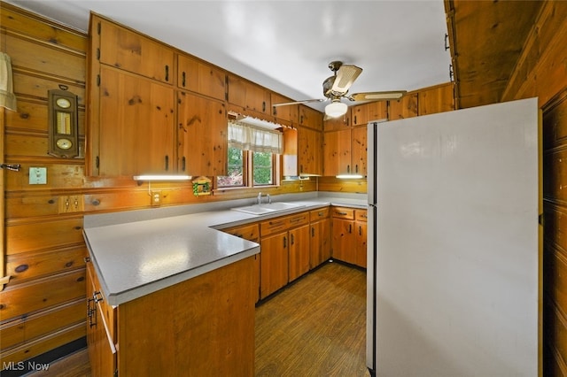 kitchen with wooden walls, hardwood / wood-style floors, sink, white fridge, and ceiling fan