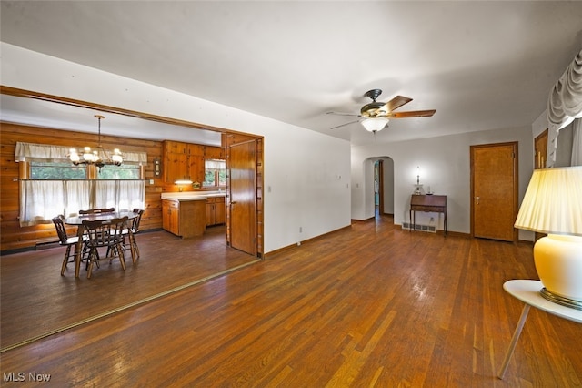 living room with dark wood-type flooring, wood walls, and ceiling fan