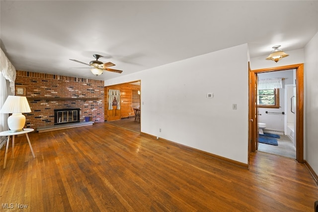 unfurnished living room featuring dark wood-type flooring, a brick fireplace, and ceiling fan