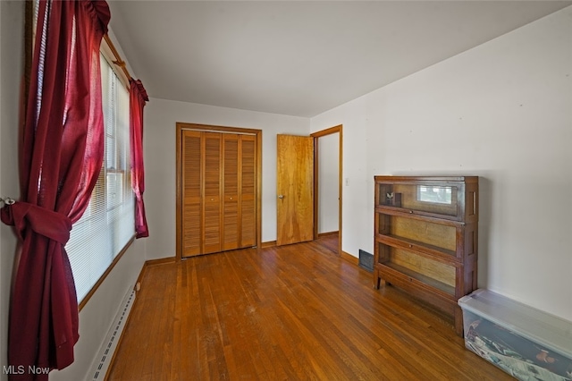 unfurnished bedroom with a baseboard heating unit, wood-type flooring, and a closet