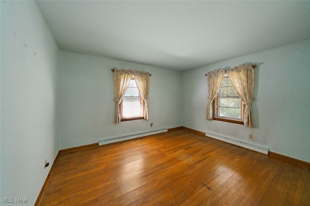 unfurnished room featuring plenty of natural light, baseboard heating, and wood-type flooring