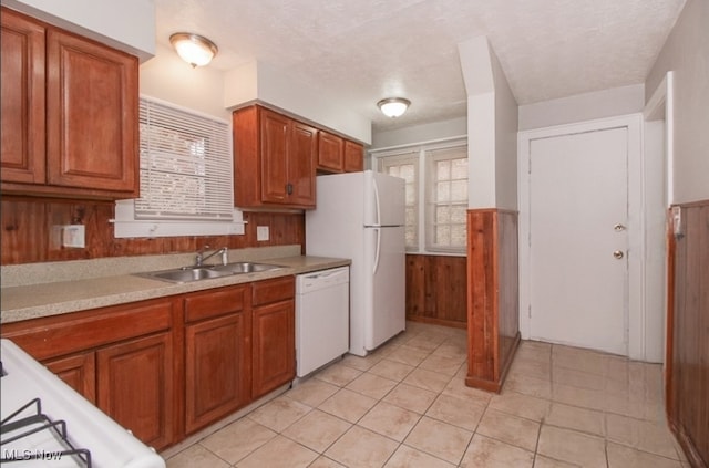 kitchen featuring light tile patterned floors, white appliances, wood walls, and sink