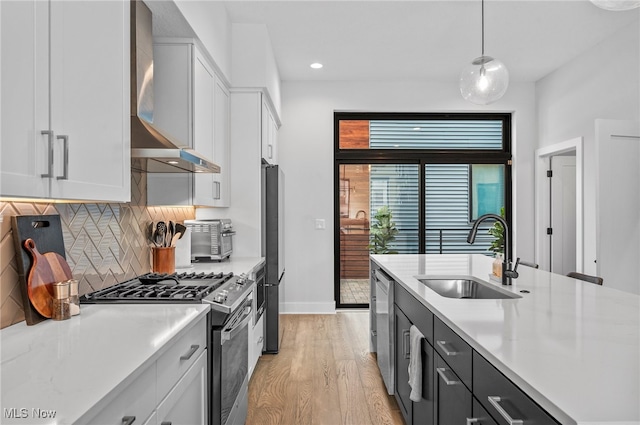 kitchen featuring wall chimney range hood, appliances with stainless steel finishes, hanging light fixtures, and white cabinets