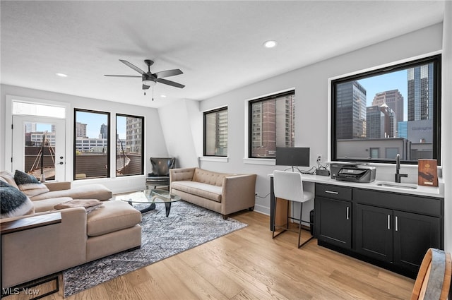 living room featuring built in desk, sink, light wood-type flooring, and ceiling fan