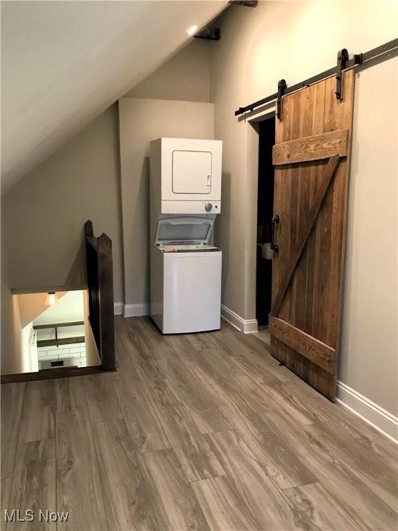 clothes washing area with a barn door, hardwood / wood-style floors, and stacked washer and clothes dryer