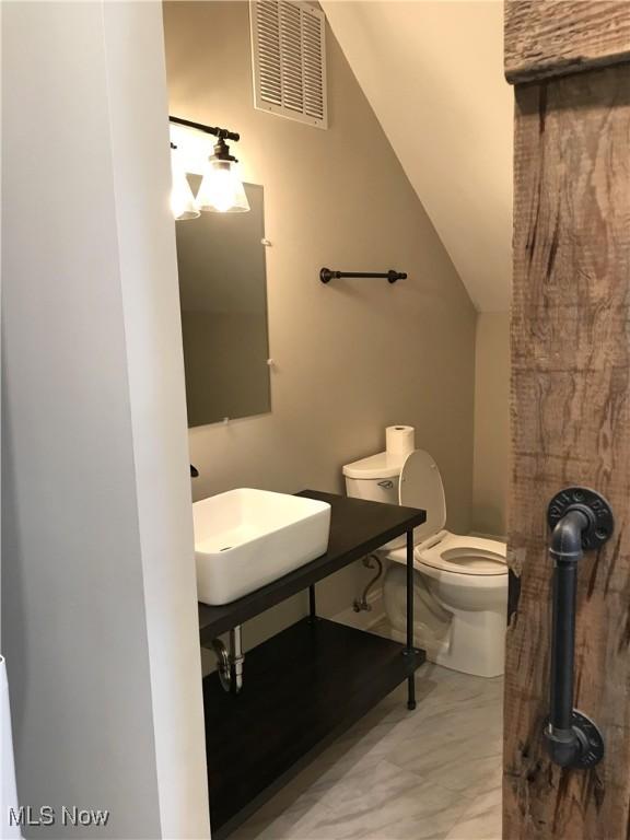 bathroom featuring toilet, sink, and lofted ceiling