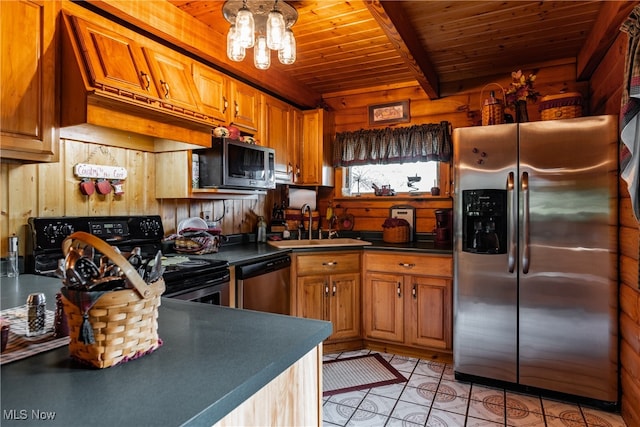 kitchen with light tile patterned floors, beam ceiling, stainless steel appliances, sink, and wooden walls