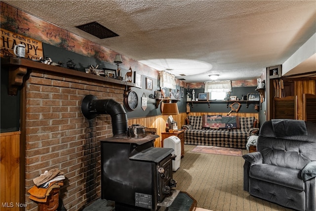 carpeted living room with wood walls, a wood stove, and a textured ceiling