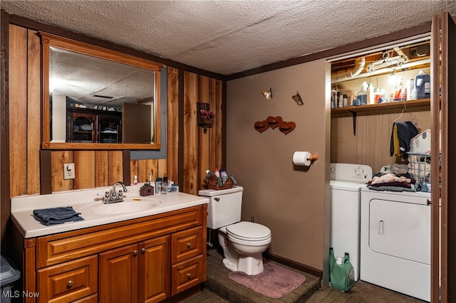 bathroom with toilet, wooden walls, separate washer and dryer, vanity, and a textured ceiling