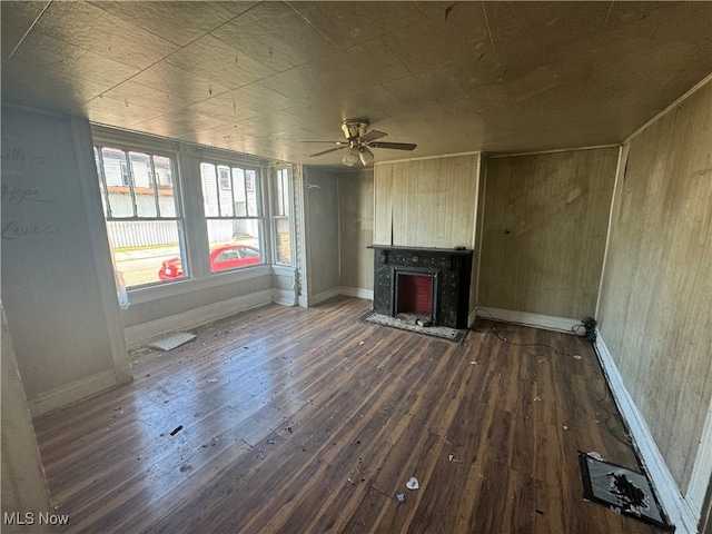 unfurnished living room featuring wooden walls, ceiling fan, and dark wood-type flooring