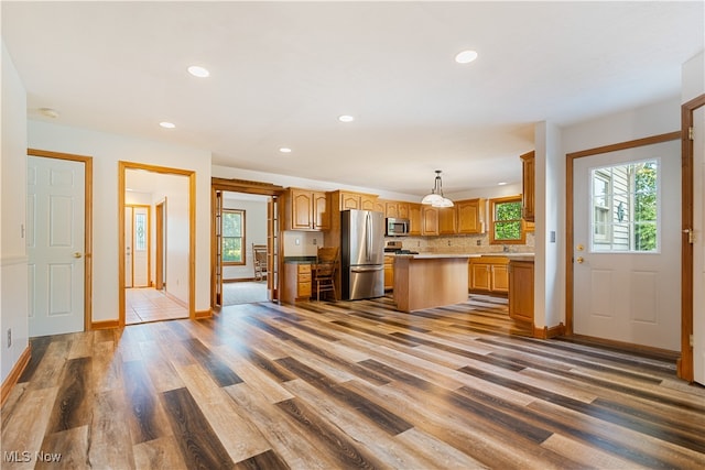 kitchen with appliances with stainless steel finishes, tasteful backsplash, pendant lighting, a center island, and hardwood / wood-style flooring