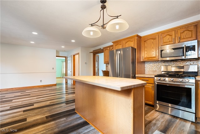 kitchen with appliances with stainless steel finishes, a kitchen island, dark hardwood / wood-style floors, and decorative light fixtures