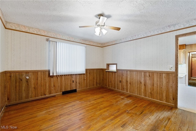 unfurnished room featuring a textured ceiling, wood-type flooring, wooden walls, and ceiling fan